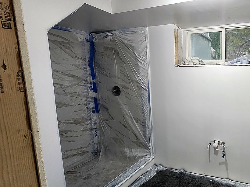 Basement bathroom with the tiled shower alcove wrapped in protective plastic sheeting during construction