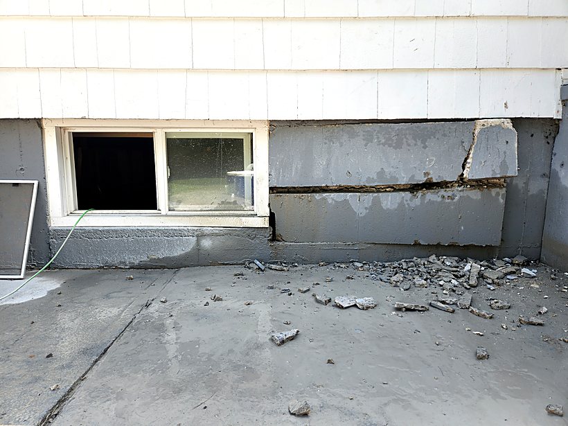 Egress window opening being cut into a poured concrete foundation wall from outside the house