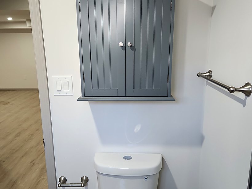 Finished basement bathroom with a grey wall cabinet, toilet and towel bar