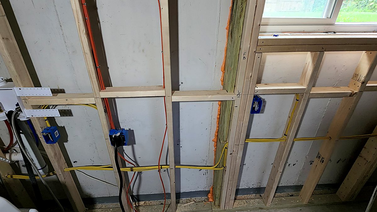 Electrical wiring and plumbing lines run through basement ceiling joists at rough-in inspection stage