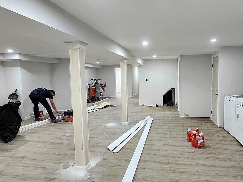 Flooring and trim being installed in a finished basement, with the laundry area visible