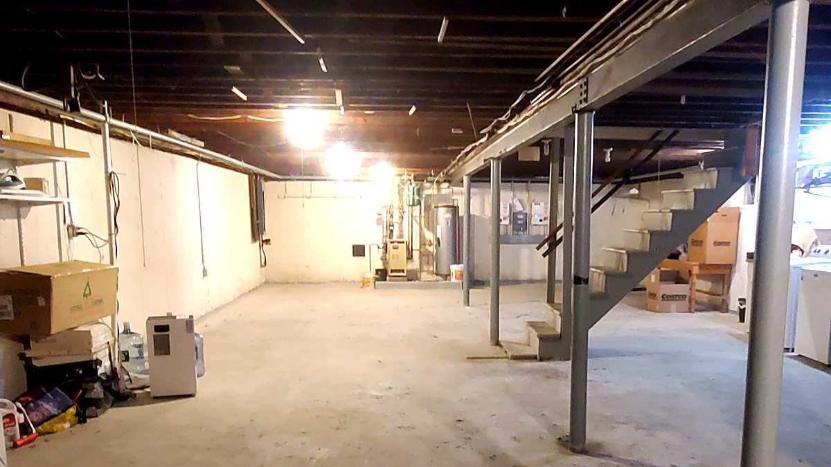 Unfinished basement before remodeling, with open ceiling joists, steel support columns and a bare concrete slab