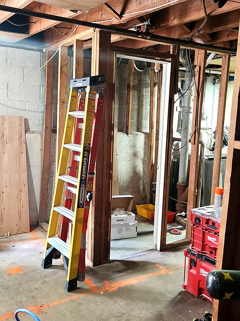 Early stage of a basement bathroom build, with stud framing up and plumbing roughed in