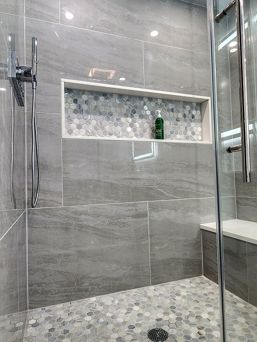Finished basement bathroom shower in Bridgeport, CT with grey tile, a pebble floor and a lit niche