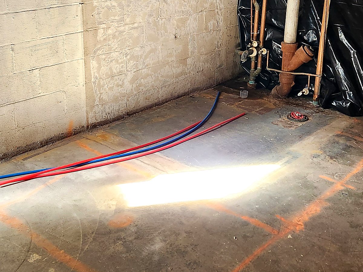 Bathroom layout marked in chalk on a bare basement slab with water supply lines and a floor drain already set