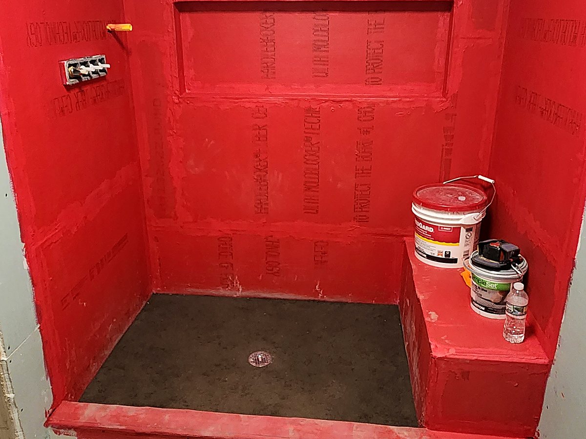 Red waterproofing membrane applied over shower walls, curb and bench before tiling, in a Bridgeport, CT bathroom build