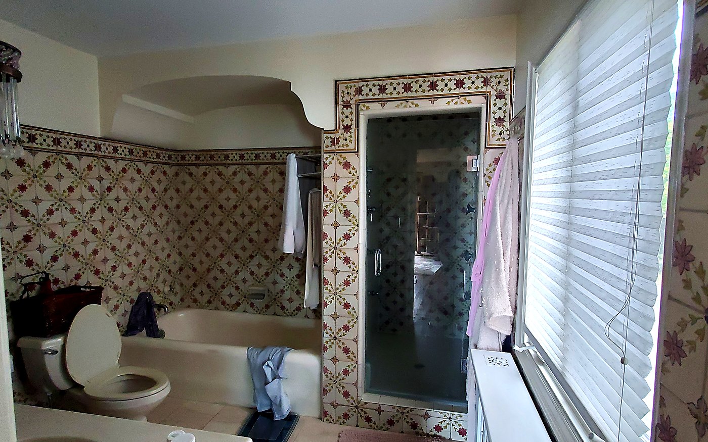 Dated master bathroom before remodeling, with ornate floral wall tile, a built-in tub and an enclosed shower stall