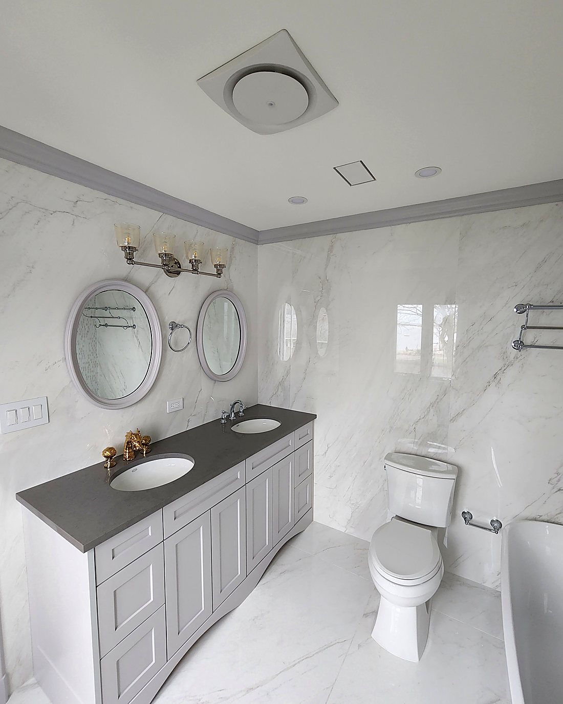 Finished double vanity in a Stamford master bathroom, with grey quartz countertop, marble-look porcelain walls and brass fixtures