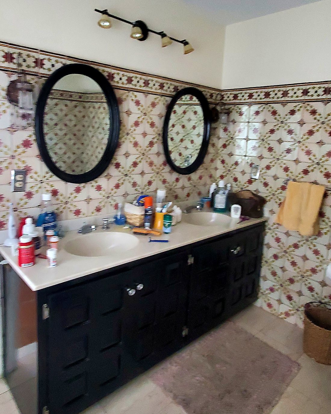 Dated master bathroom vanity before remodeling, with patterned ceramic tile and a black double vanity