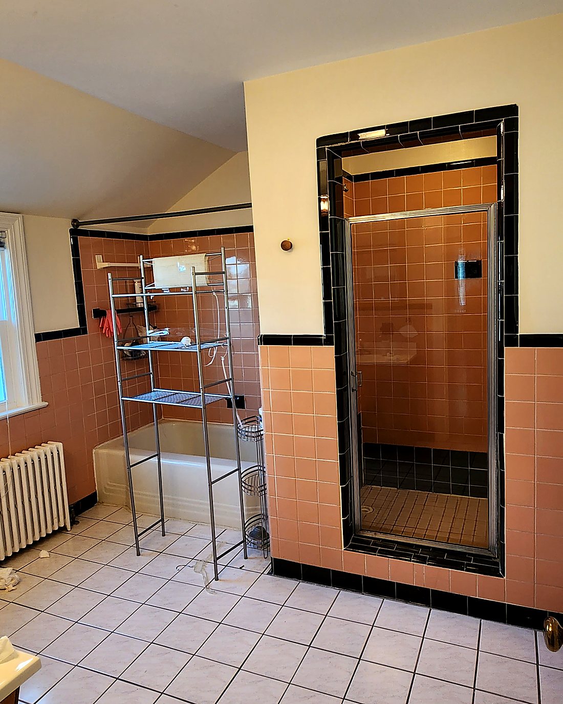 Dated bathroom before remodeling, with salmon wall tile, black trim and an enclosed shower stall