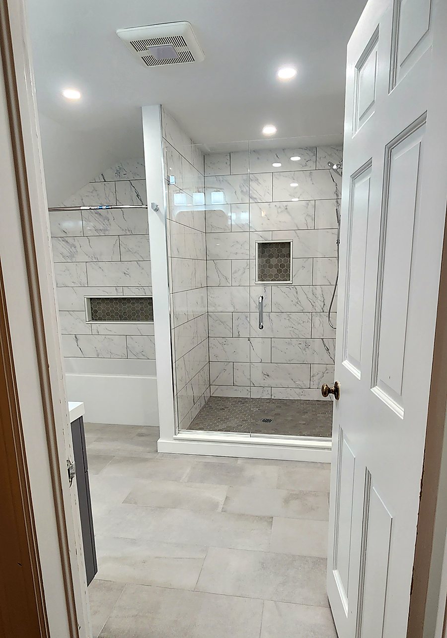 Finished walk-in shower in marble-look porcelain tile with a recessed niche and a clear glass panel