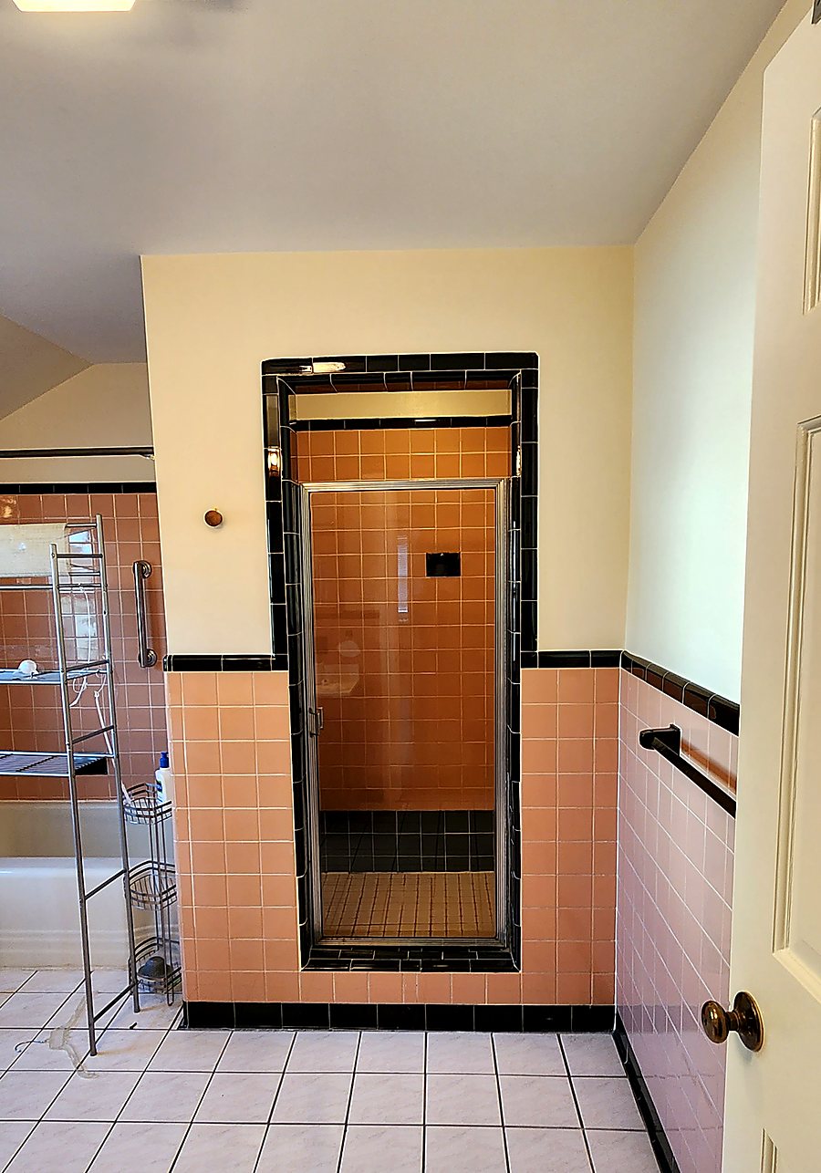 Old enclosed shower stall with a bronze glass door and salmon tile before remodeling