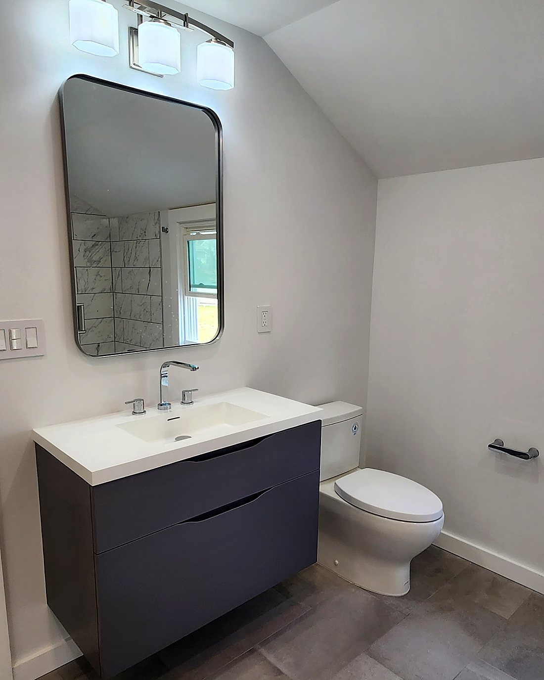 Finished bathroom vanity in Mid-City Stamford with a wall-hung charcoal vanity, integrated basin, black-framed mirror and modern sconce