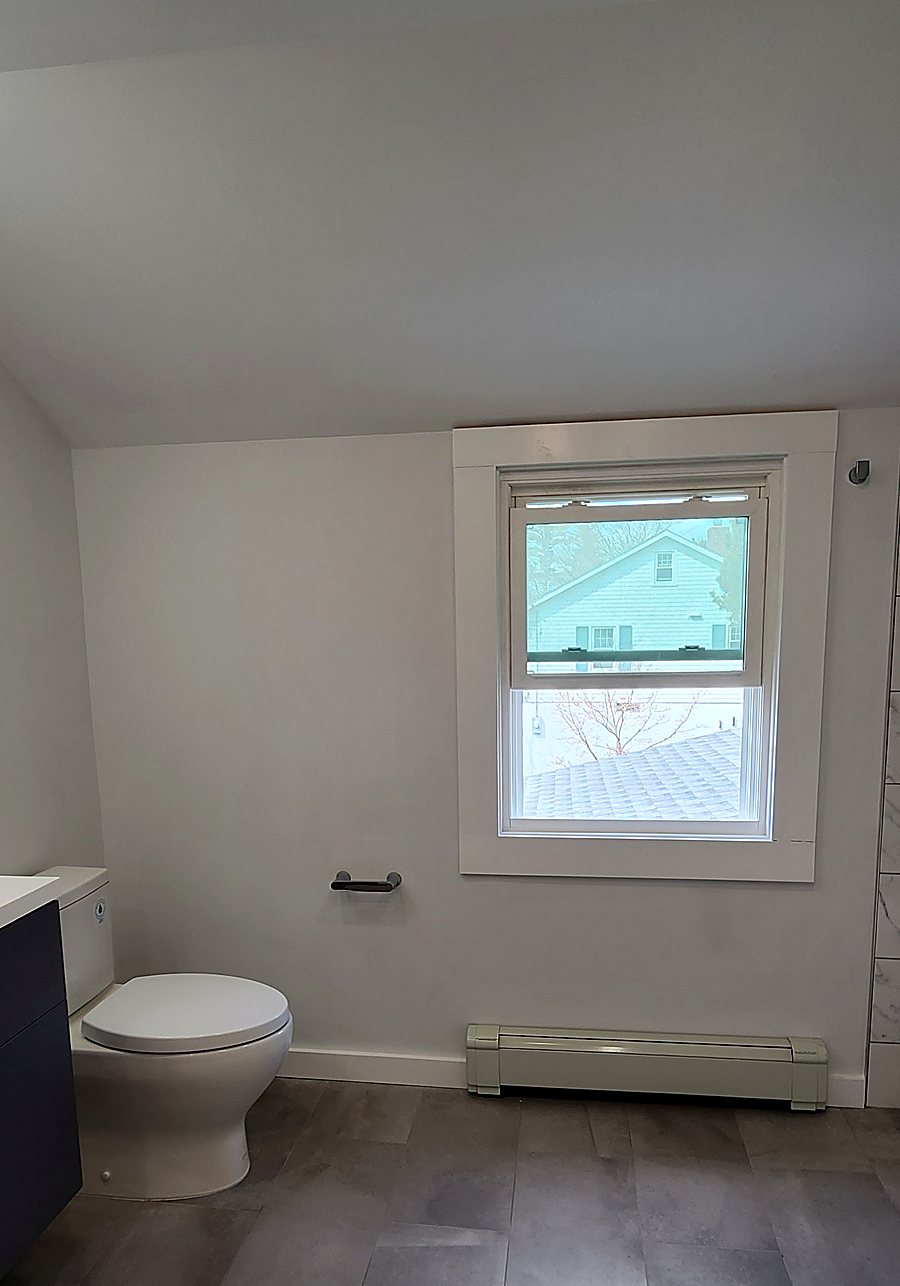 Finished window wall in a Mid-City Stamford bathroom with a new toilet, baseboard heating and porcelain floor tile