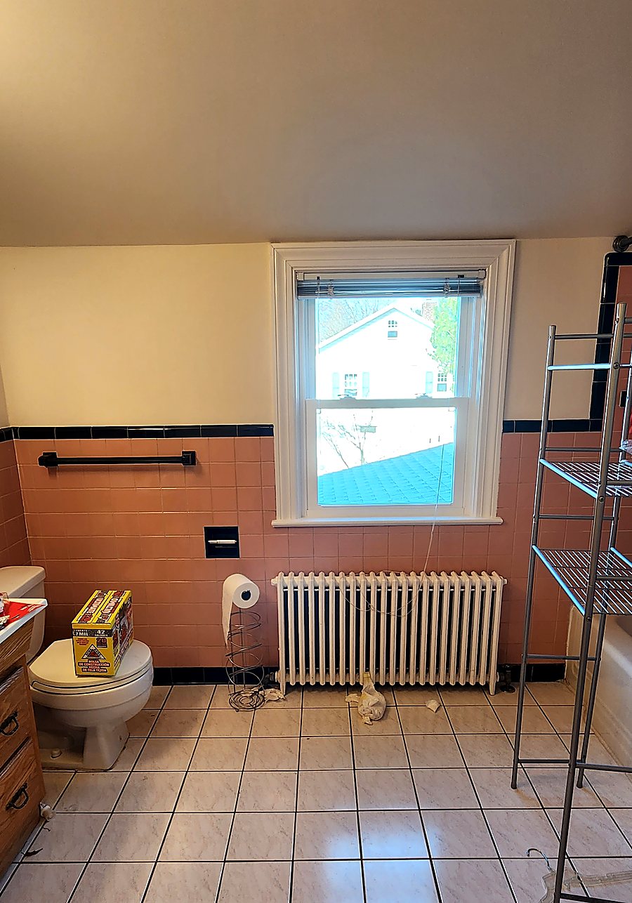 Dated bathroom window wall before remodeling, with salmon tile, an exposed radiator and old fixtures